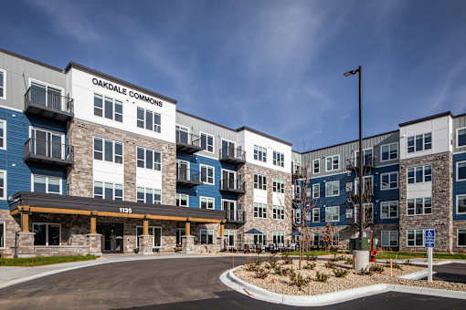 The image shows a multi-story residential building named Oakdale Commons with a parking lot in front.