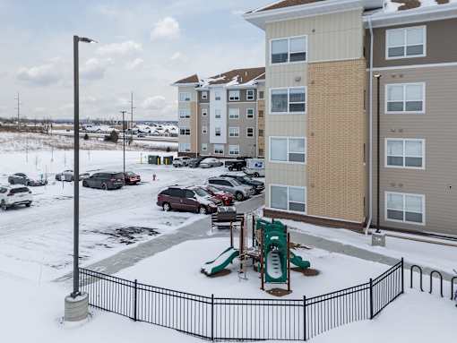 A playground in a snowy parking lot in front of apartment buildings.