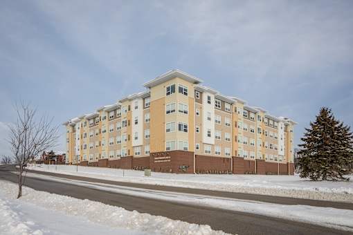 A large apartment building with a brown fence and a tree in front of it.