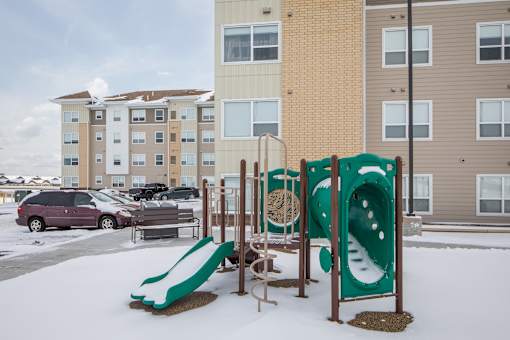 A playground with a green slide and a brown and tan building in the background.