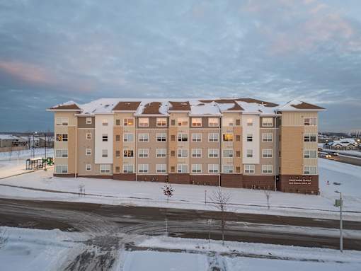 A large apartment building with snow on the roof and ground.