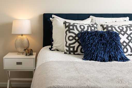 A bed with a white comforter and a blue pillow with a black pattern.
