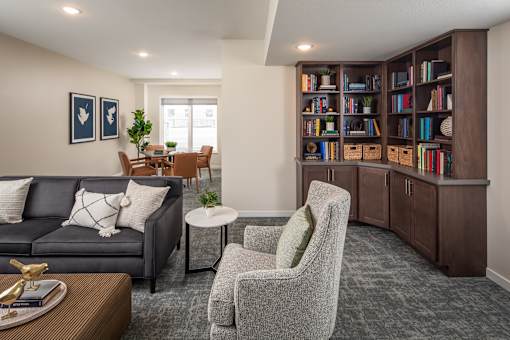 A living room with a grey sofa, a grey armchair, a coffee table, and a bookshelf filled with books.