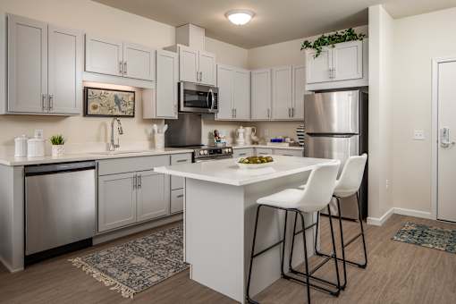 A kitchen with white cabinets and a white island with two chairs.