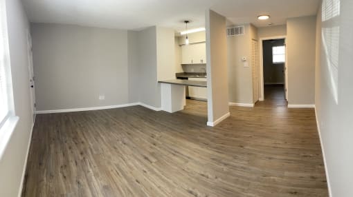 an empty living room with wooden floors and a kitchen