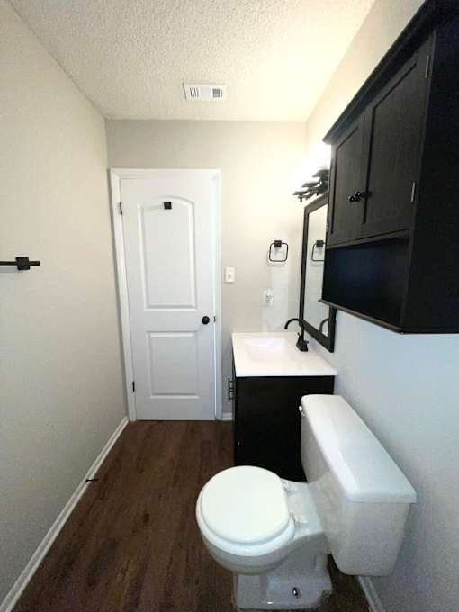 A white toilet sits in a small bathroom with a black cabinet and a white door.