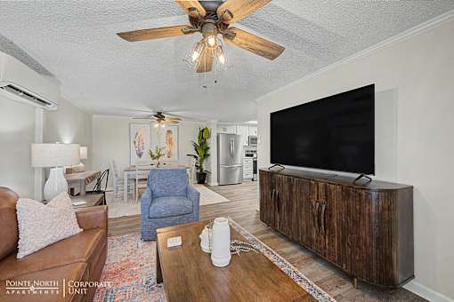 A living room with a brown couch, a blue chair, a wooden coffee table, and a flat screen TV mounted on the wall.