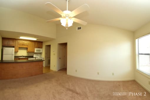 an empty living room with a ceiling fan and a kitchen