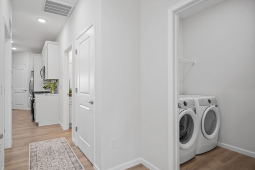 a white laundry room with washer and dryer and a door to a kitchen