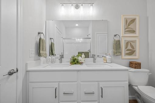 A white bathroom with a double sink and a toilet.