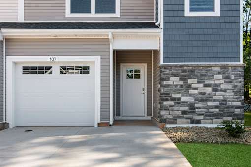 A house with a white garage door and a stone wall.