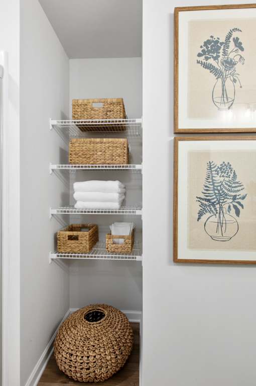 A bathroom with a white wall and a shelf with baskets and towels.