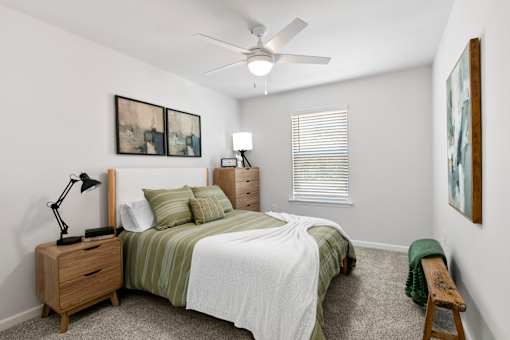 A bedroom with a bed, nightstand, and a window with blinds.