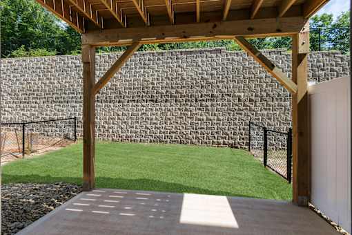 A wooden pergola over a concrete patio with a stone wall in the background.