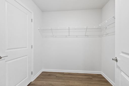 A white closet with a wooden floor and a white door.