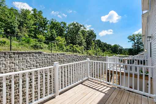 A white railing on a wooden deck overlooks a forest.