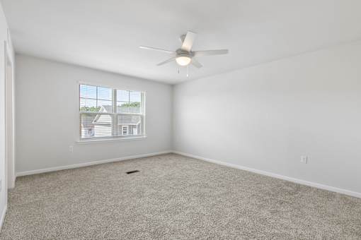 A room with a ceiling fan and a window showing a house.