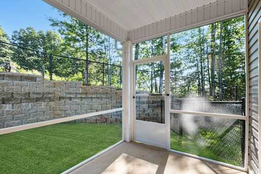A white door is open to a backyard with a green lawn and a stone wall.