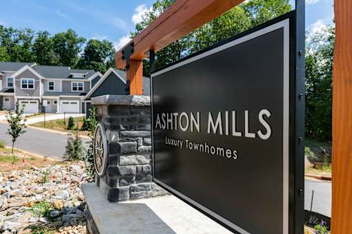 A sign for Ashon Mills Luxury Townhomes stands in front of a house.