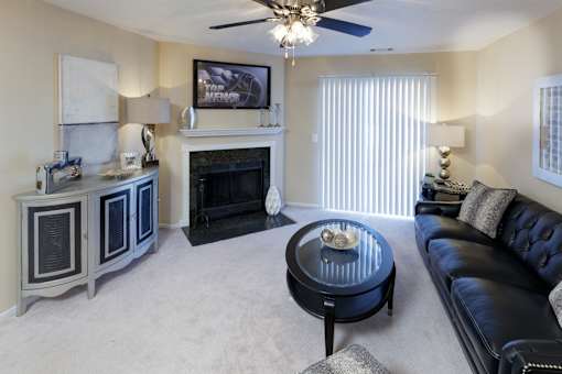 A living room with a black leather couch, a fireplace, and a ceiling fan.