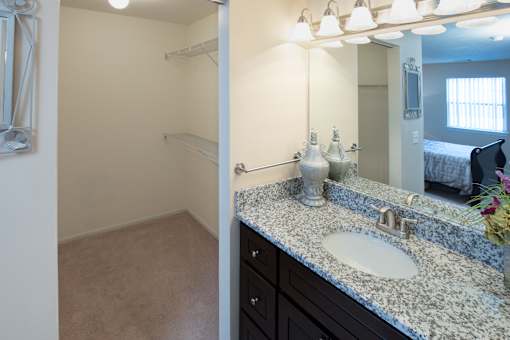A bathroom with a sink, mirror, and a bed in the background.