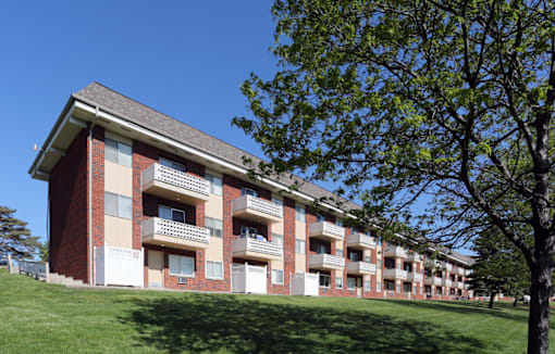 A red brick apartment building with a green tree in front.