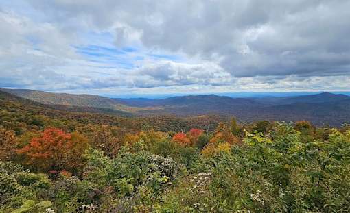 A landscape image of a mountain range with autumn trees in the foreground.