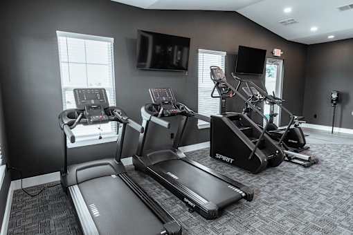 A gym with treadmills, elliptical machines, and a television.