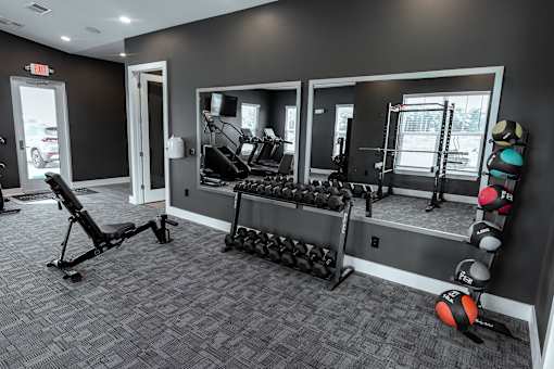 A gym with a variety of equipment including a squat rack, dumbbells, and a bench press.