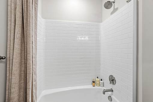 A white tiled bathroom with a shower and a white bathtub.