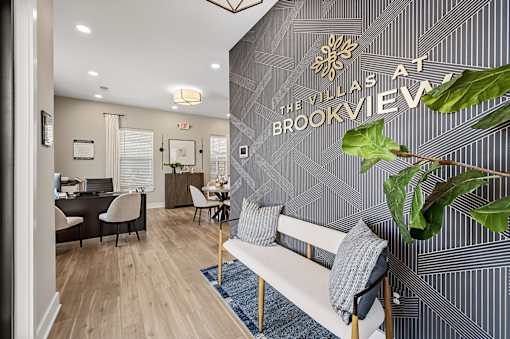 A living room with a couch and a plant in front of a wall with a sign that says "Villas at Brookview".