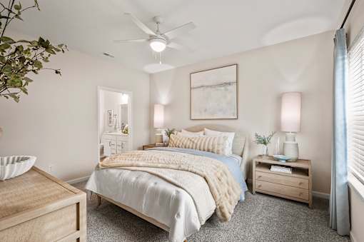 A bedroom with a bed, nightstand, and a plant.