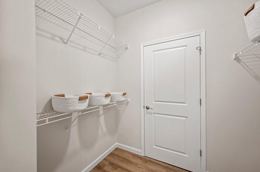 A white pantry with a white door and shelves with bowls on them.