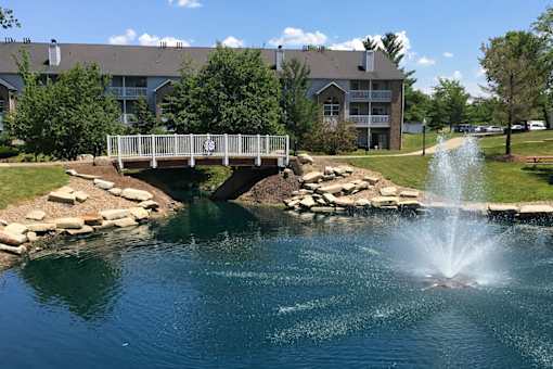 A bridge over a pond with a fountain in the middle of it.