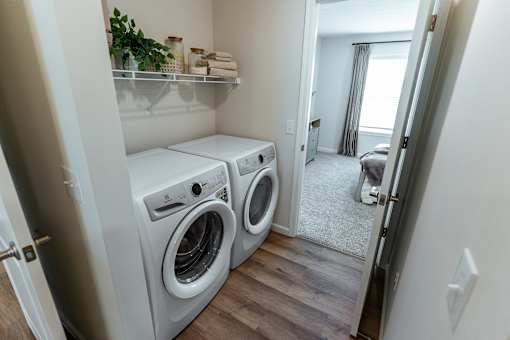 A laundry room with two washing machines and a shelf with towels and plants.