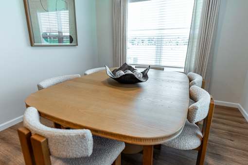 A round wooden table with a hat on it and chairs around it.