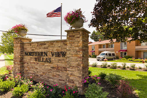 A sign for Northern View Villas is surrounded by flowers and an American flag.