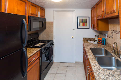 A kitchen with a black refrigerator, black microwave, black oven, and a white door.