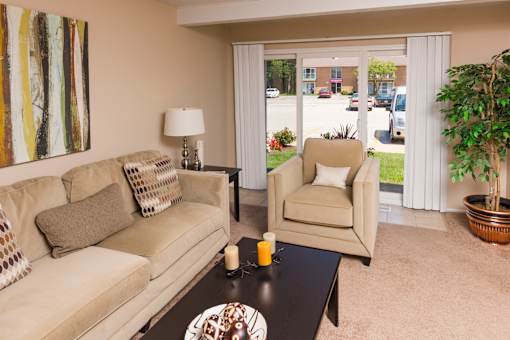 A living room with a beige couch, a chair, a table with a candle, and a painting on the wall.