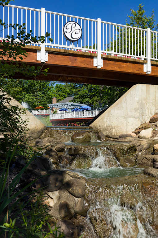 A bridge with a logo on it spans over a small waterfall.