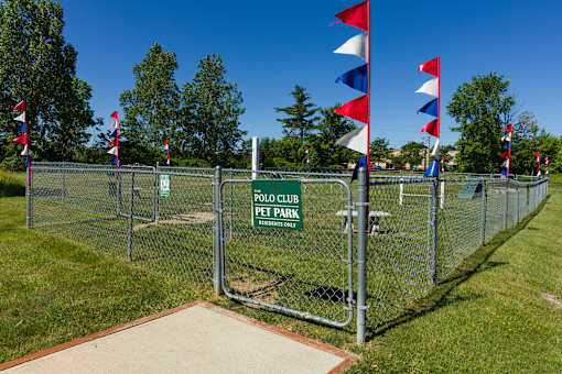 A fenced area with flags and a sign that says "Polo Club Pet Park".