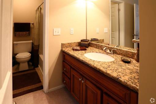 A bathroom with a granite counter top and a toilet in the corner.