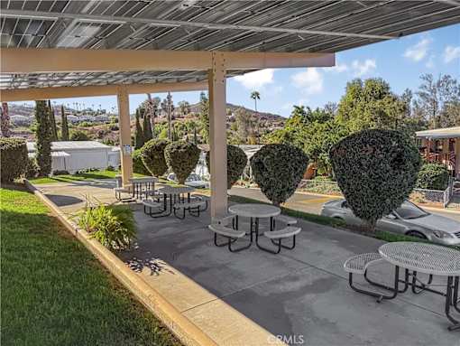 A patio with tables and chairs under a roof with trees in the background.