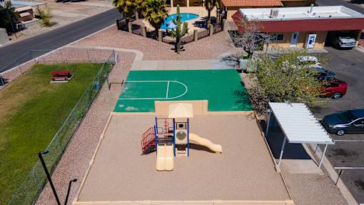 A basketball court is surrounded by a green fence and a playground.