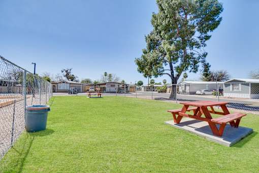 A red picnic table sits on a concrete slab in a grassy park.