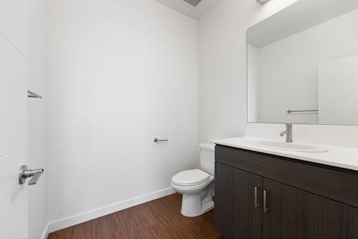 A white toilet sits in a bathroom with a wooden floor and white walls.