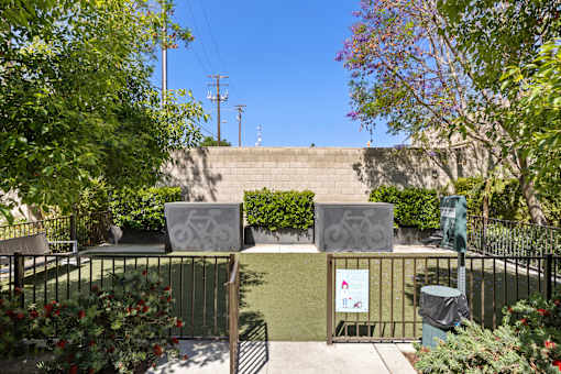 A sign with a bicycle symbol is attached to a fence in a green space.