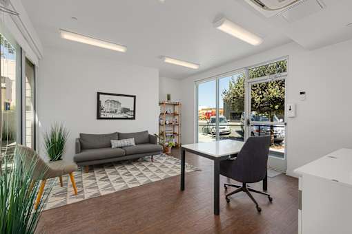 A modern office space with a grey sofa, a black chair, and a framed picture on the wall.