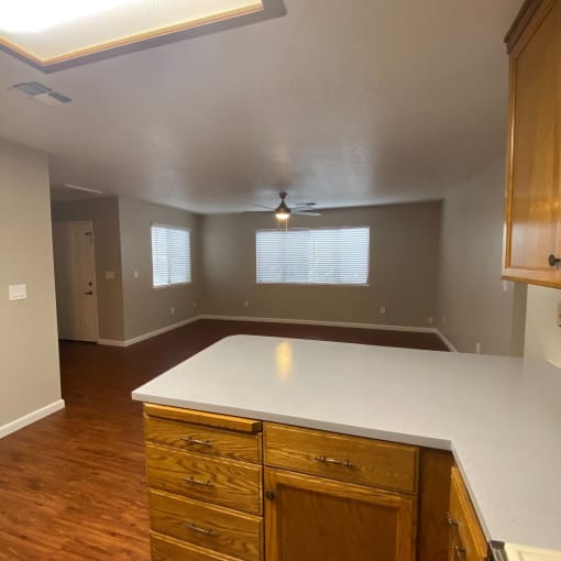 an empty kitchen with a white counter top and wooden floors