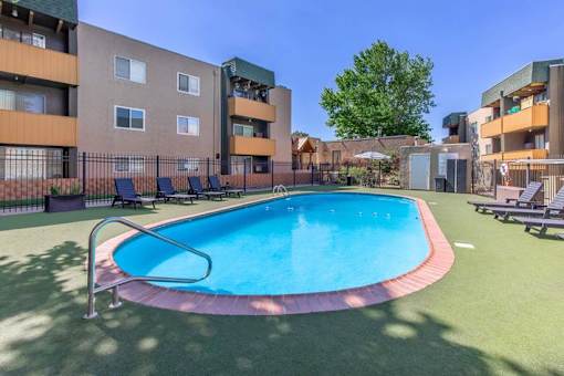 A swimming pool surrounded by a fence and chairs in front of apartment buildings.